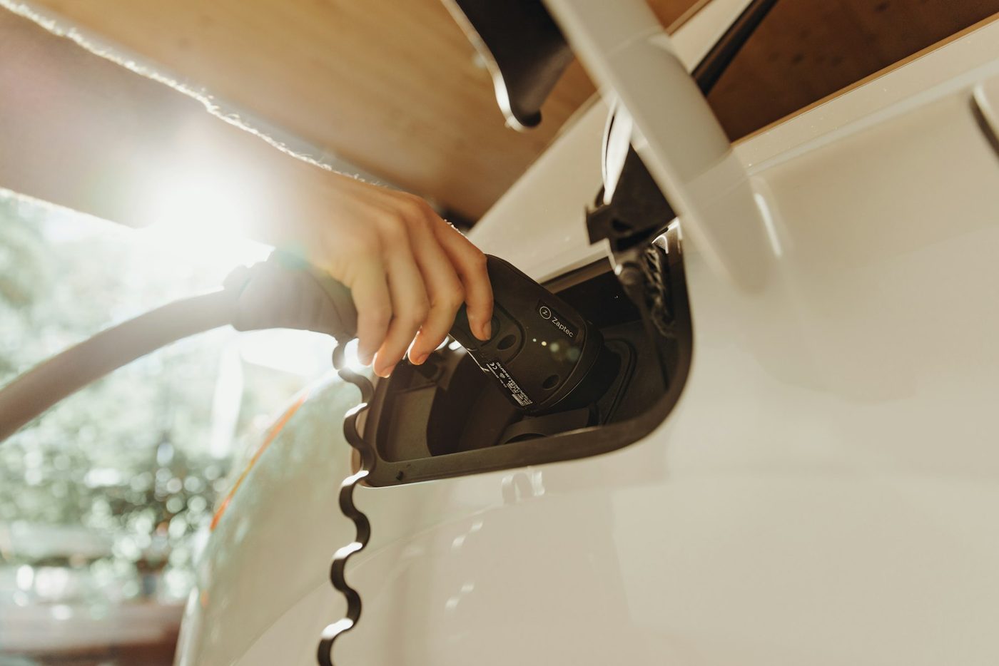 A hand plugging a charging cable into an electric car